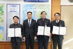 2026년 상반기 4급이하 정기인사로 정장을 입은 남성 세 명과 상장을 받은 남성 한 명이 실내 사무실 대형 지도 앞에서 기념 촬영을 하고 있으며, 양끝의 남성 두 명은 각각 펼쳐진 임용장을 양손으로 들고 정면을 응시하고 있다.